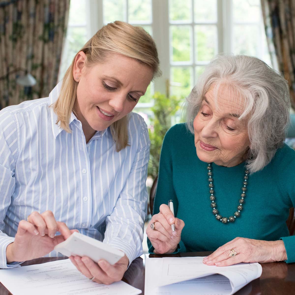 An adult daughter helps her senior mom review financial documents.