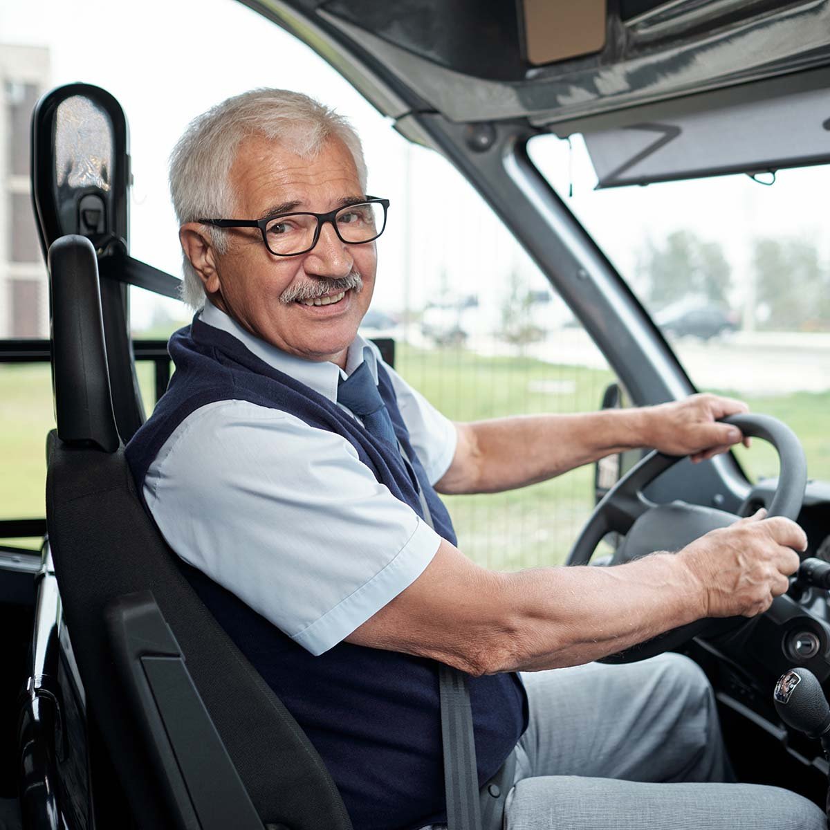 Bus driver smiling while in the driver's seat of a bus.