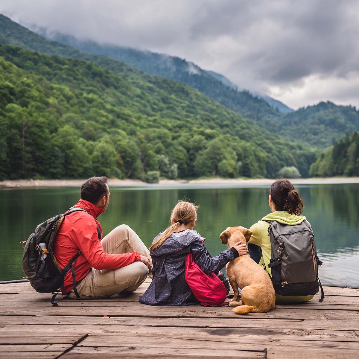 A family of four sits on a dock near a mountain lake while on vacation.