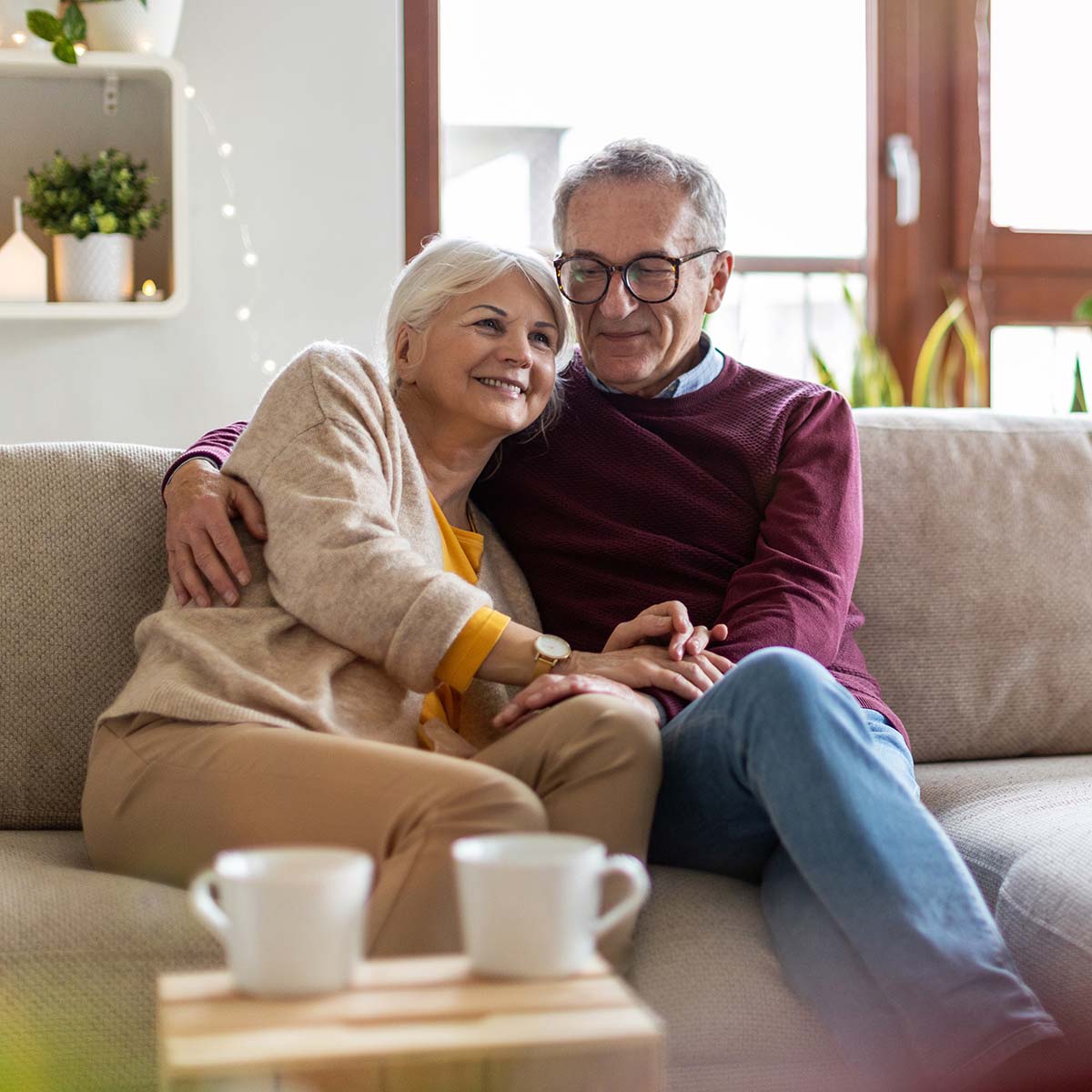 A senior couple smile together while having coffee at their couch.