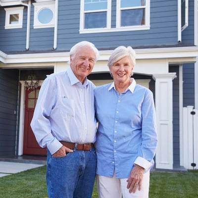 senior-couple-standing-in-front-of-house-1200x1200