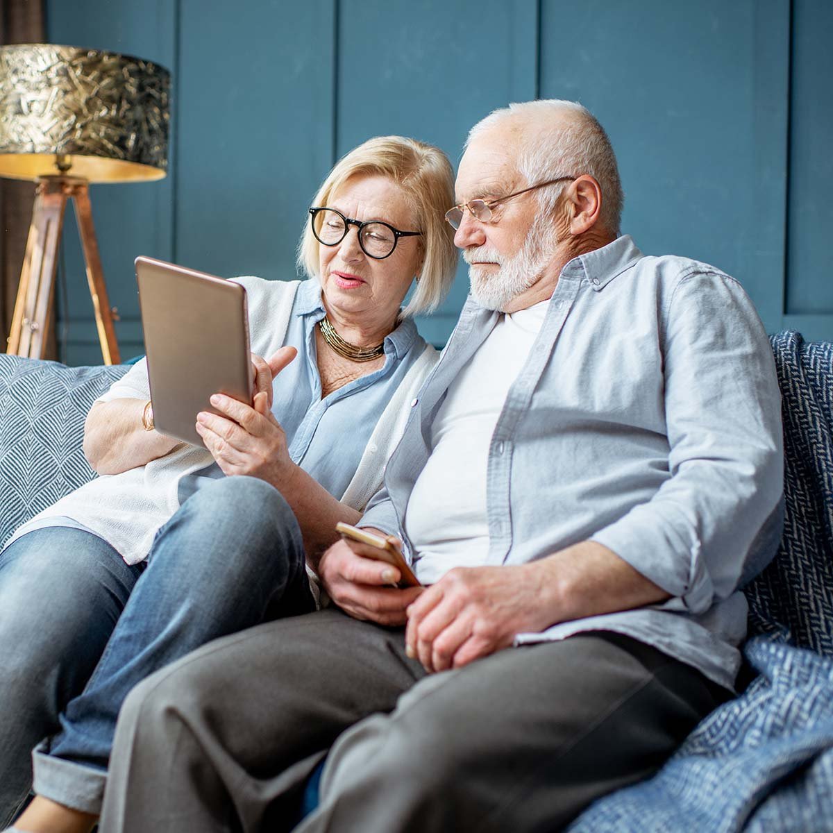 A senior couple uses a tablet while sitting together on a couch.