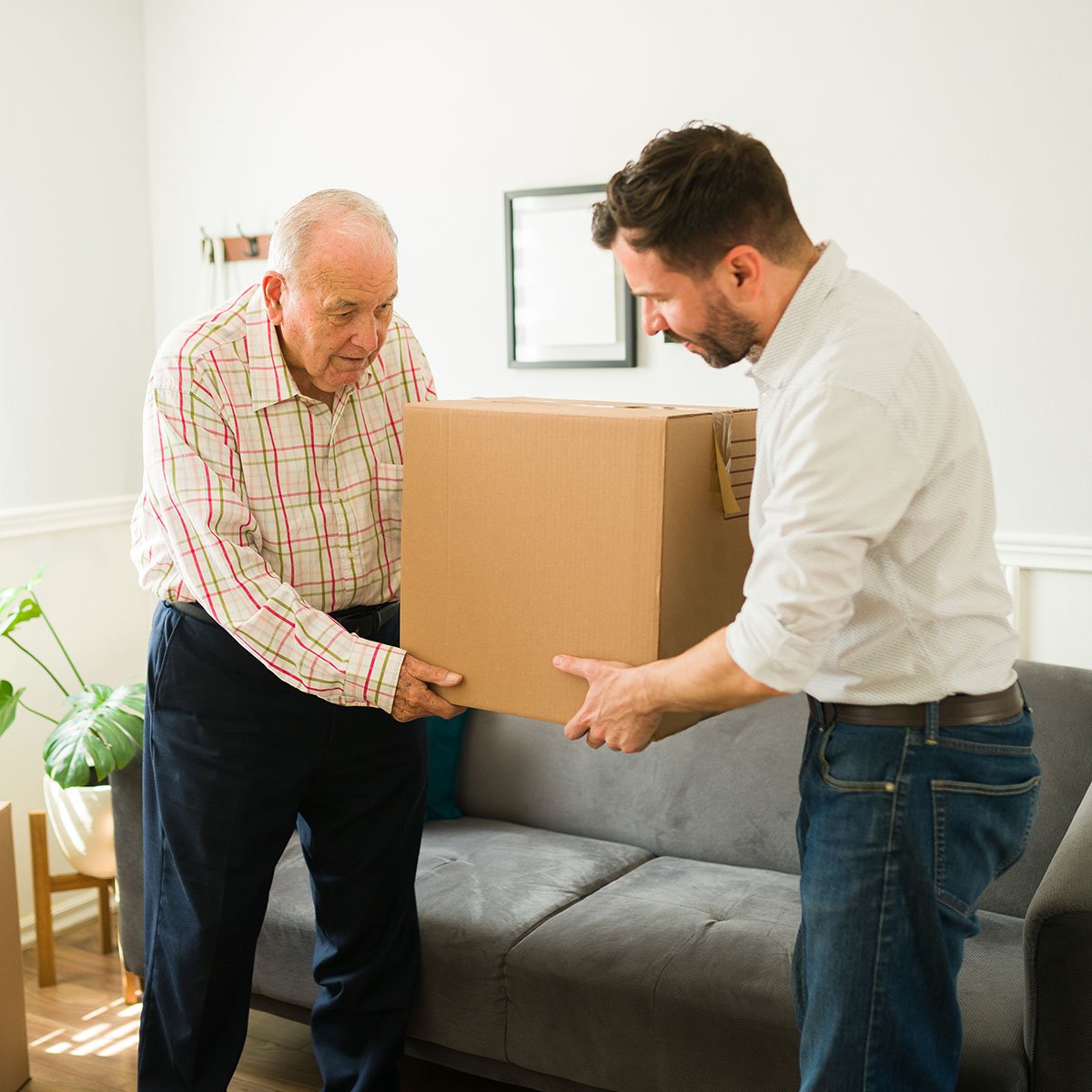 A senior man and his adult son lift a moving box.