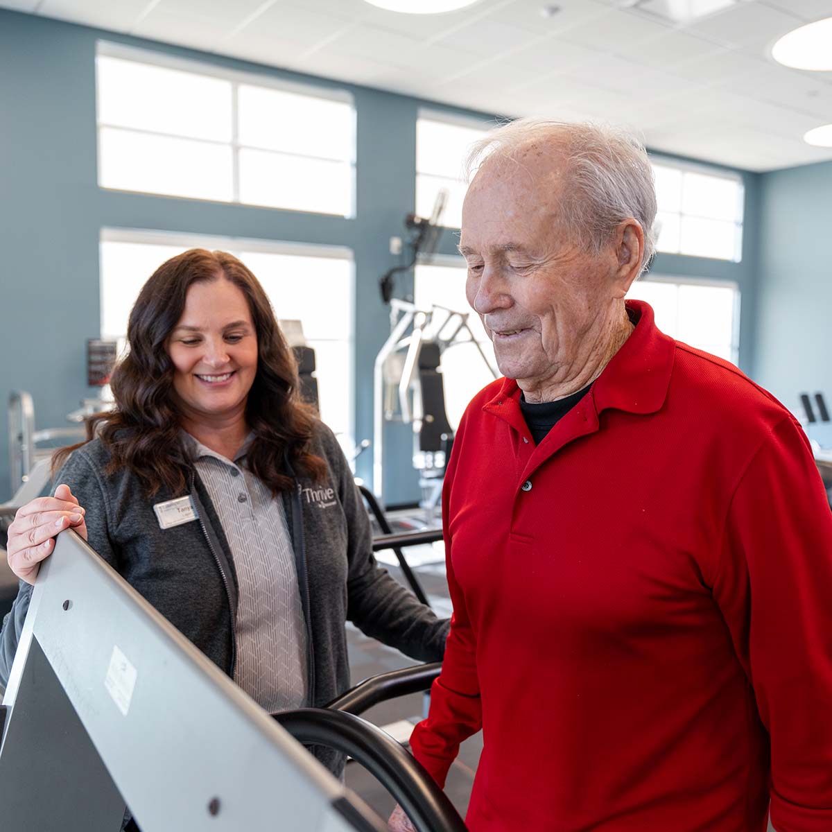A Thrive instructor works with a resident as they are walking on a treadmill.
