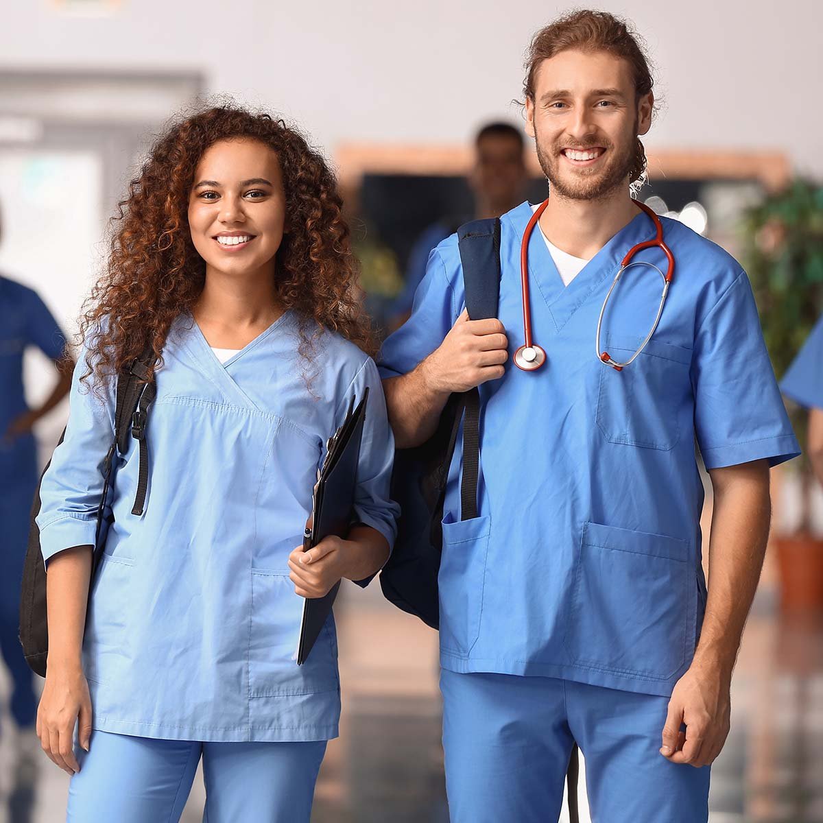 Two student nurses smile while standing in a hallway.