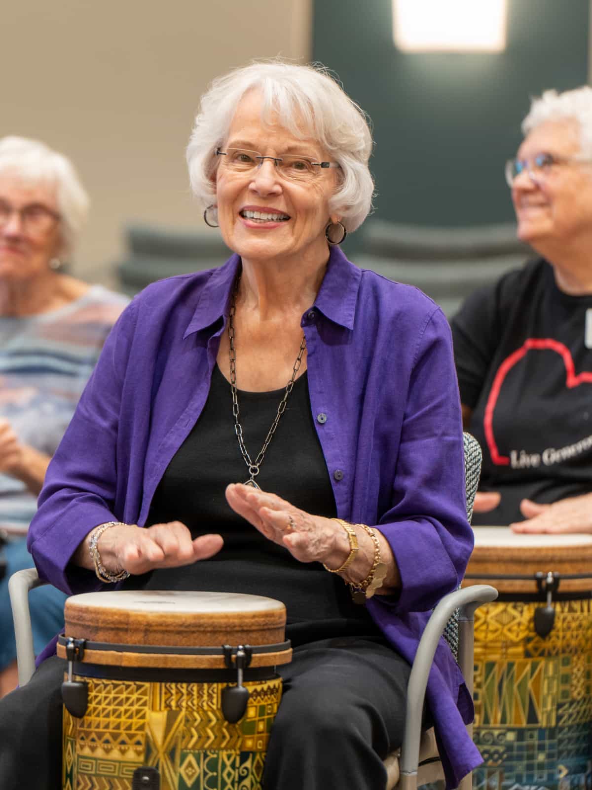 Senior woman smiles while playing a hand drum.