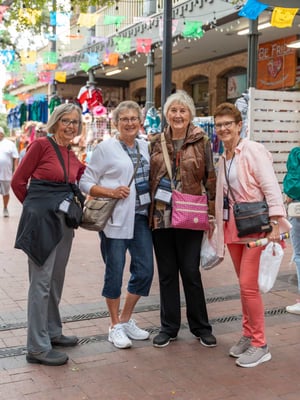 A group of seniors smile and embrace as they are shopping in a market.