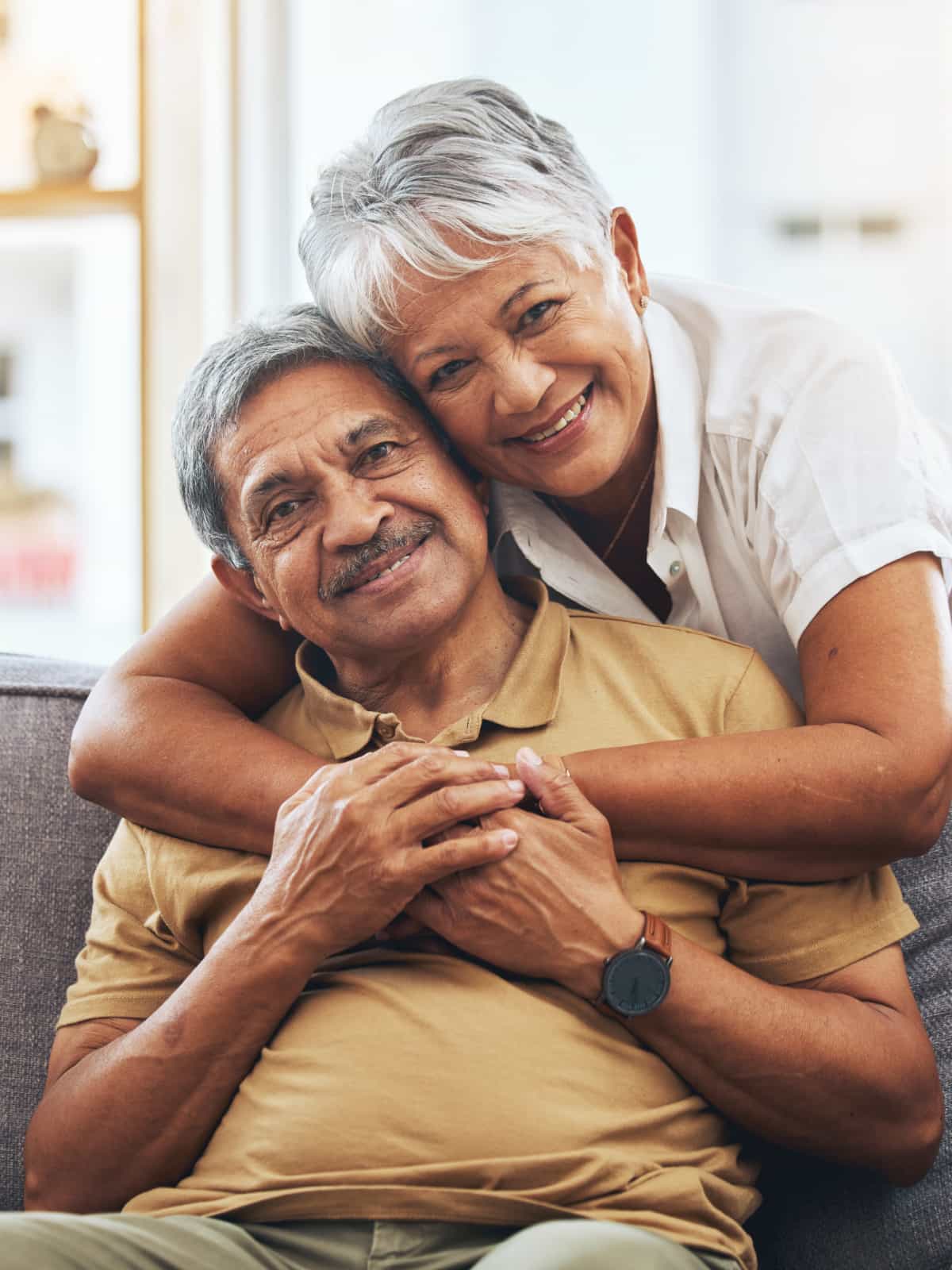 A happy senior couple embrace on their living room sofa.