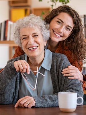 A senior grandma smiles as her granddaughter embraces her.