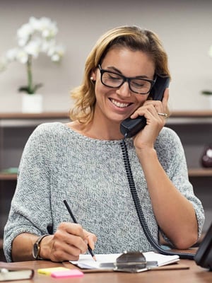 A woman smiles while talking on an office telephone.