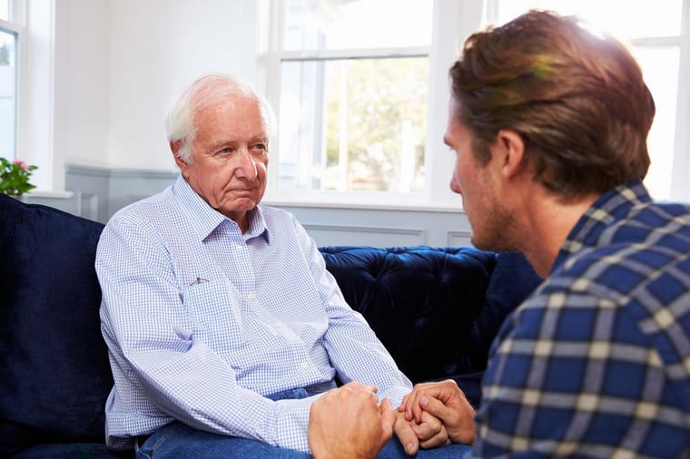 Adult son holds senior father's hands.