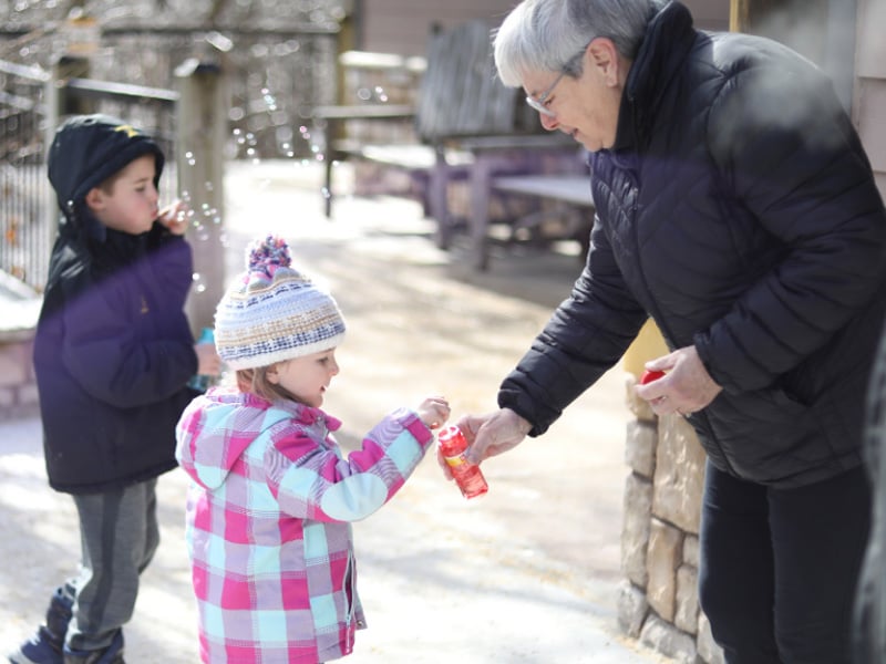 A woman helps a young girl with some bubbles.
