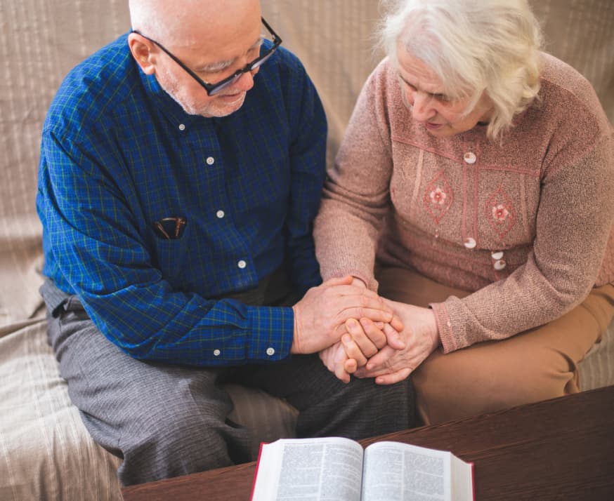 A senior couple hold hands as they pray together.