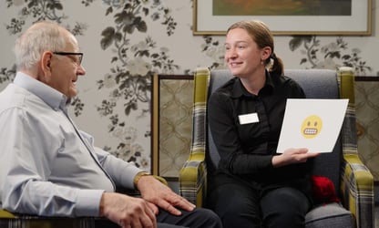 An employee holds up a piece of paper with an emoji for a resident to guess what it means.