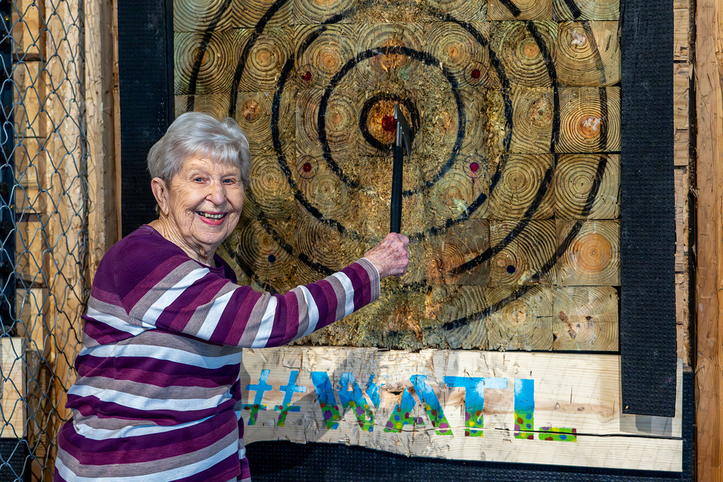 A senior woman smiles with an Axe Throwing bullseye