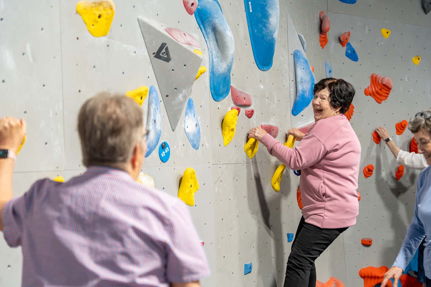 A senior woman climbs an indoor rock wall.