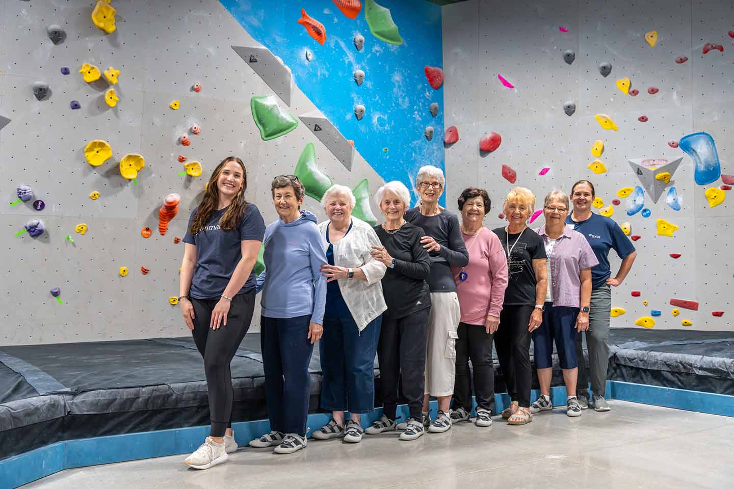 A group of seniors pose for a photo in front of a rock climbing wall.