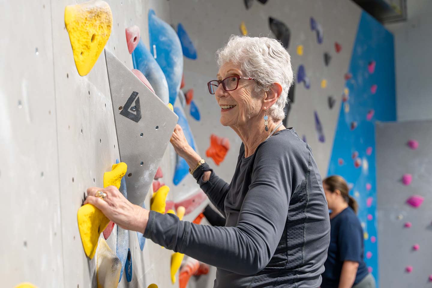 A senior woman climbs an indoor rock wall.