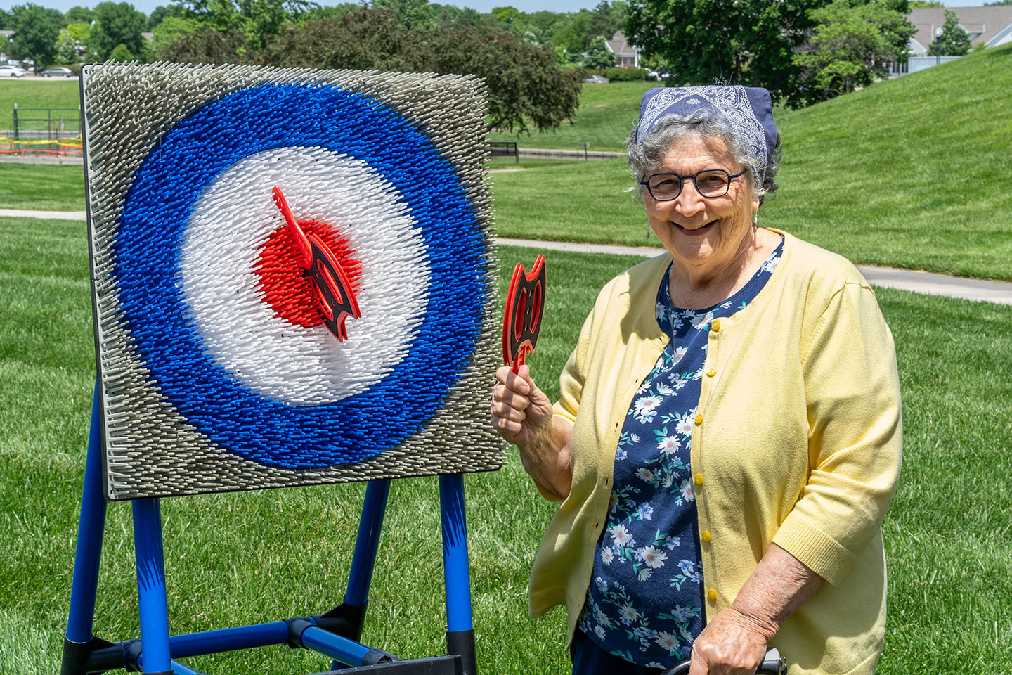 A senior woman celebrates a bullseye in a yard axe throwing game.