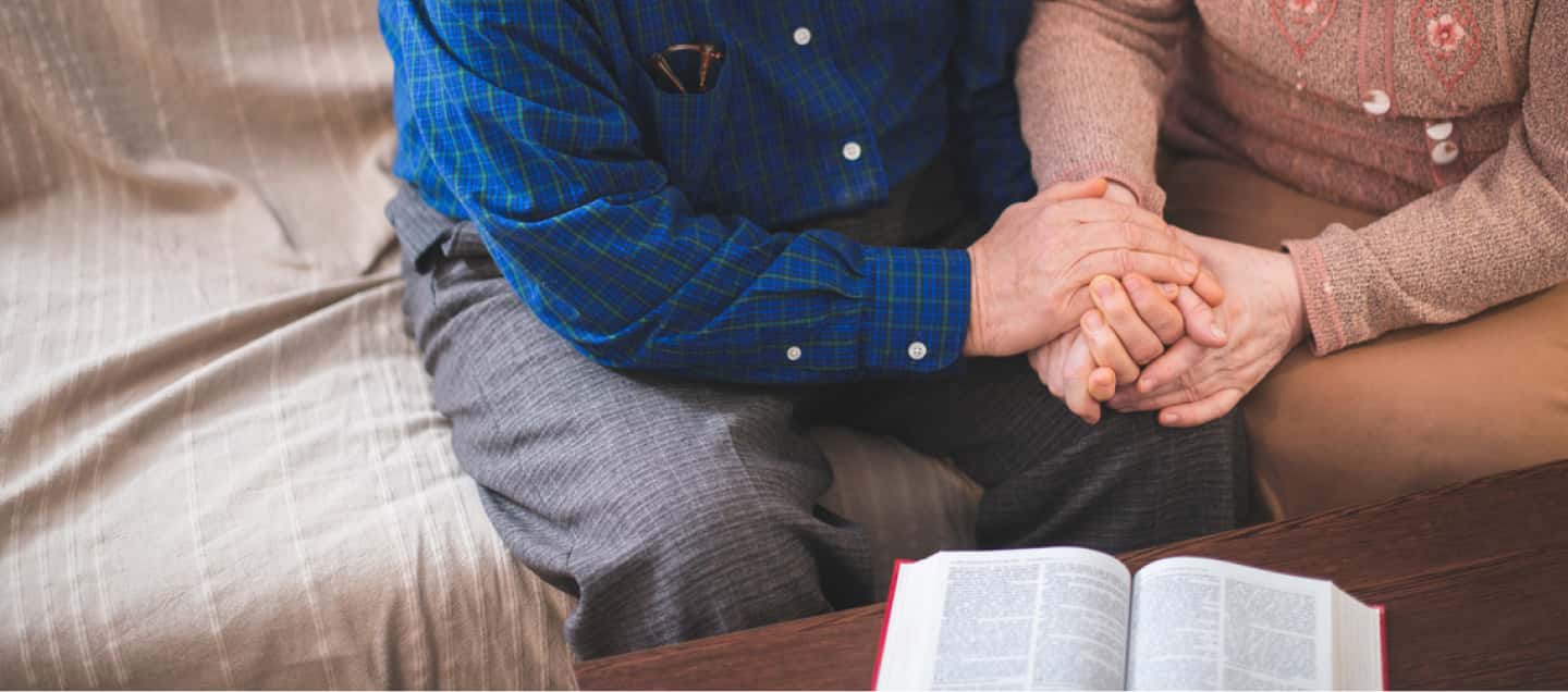 Elderly couple holding hands while reading the bible.