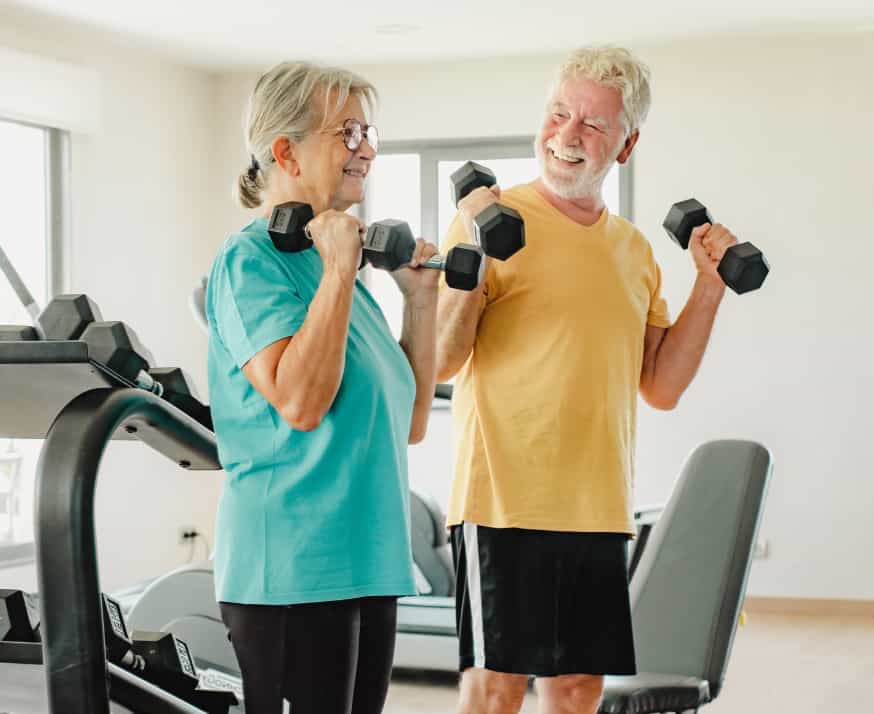 Senior couple in sportswear exercising with dumbbells in a wellness center.